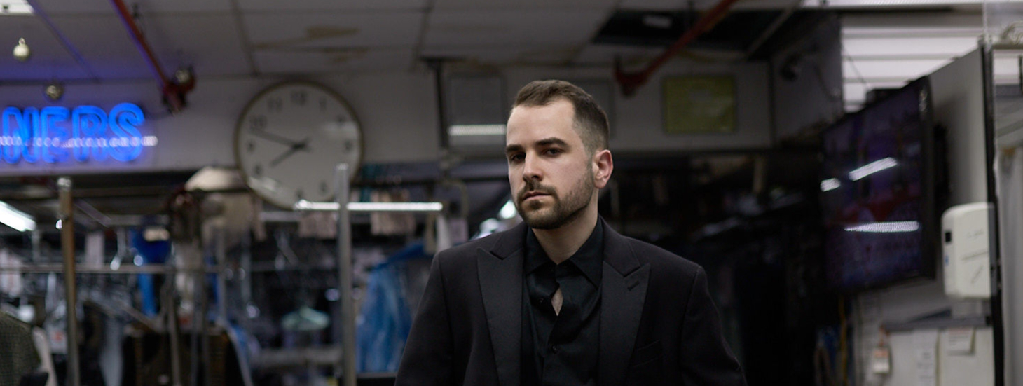 Josh Popkin in a black suit, editorial portrait in a New York dry cleaners