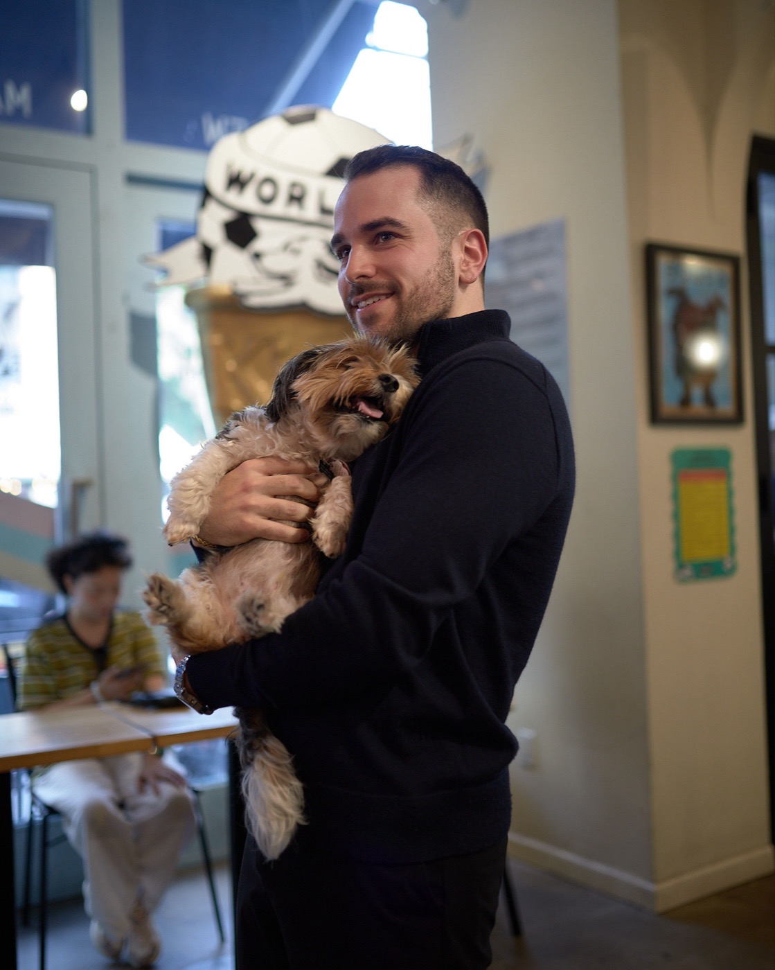 Josh Popkin smiling and holding his dog in a New York City café